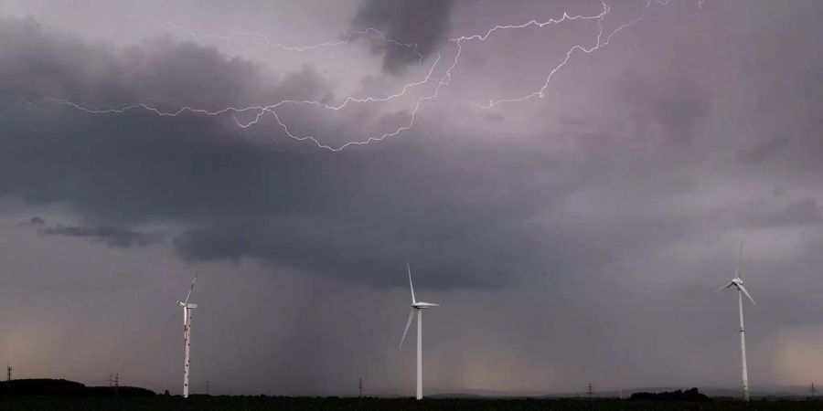 Eine Unwetterfront mit Blitzschlag zieht über ein Feld mit Windrädern hinweg.