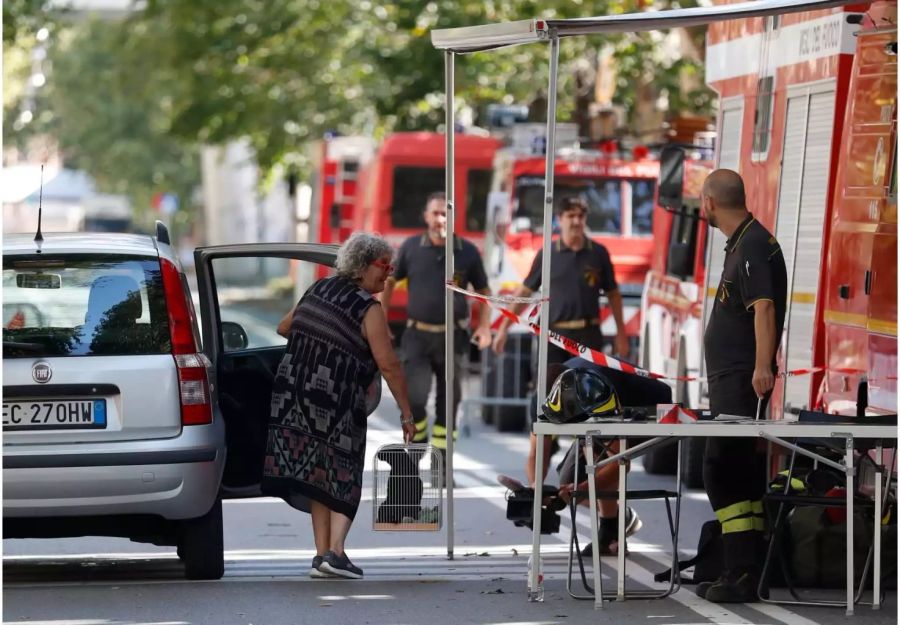 Eine Frau spricht mit Feuerwehrleuten. Die Feuerwehrleute begleiten Bewohner in ihre evakuierten Häuser, damit diese ihre Habseligkeiten holen können.