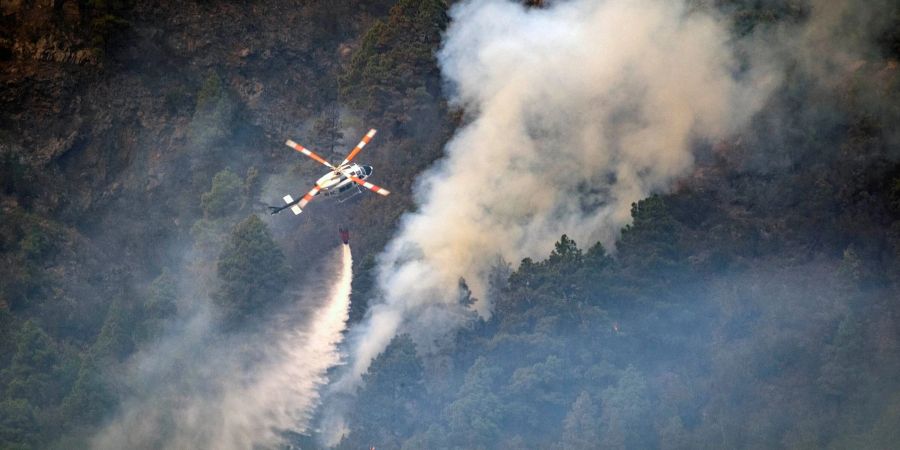 Ein Hubschrauber wirft Wasser auf die Flammen, während sich das Feuer durch den Wald in Richtung der Stadt Pinolere ausbreitet.