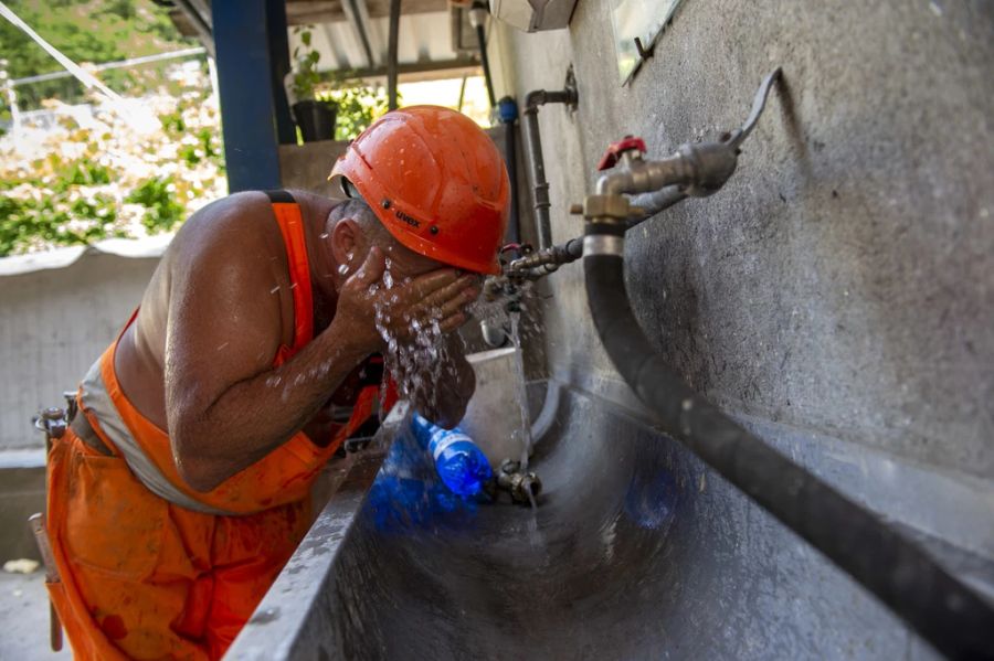 Dieser Bauarbeiter kühlt sich unter einem Wasserhahn.