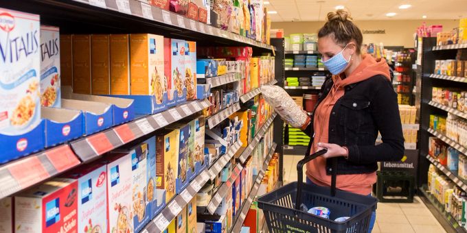 Die Maskenpflicht im Einzelhandel ist mittlerweile Vergangenheit. Dennoch tragen viele den Mund-Nasen-Schutz weiterhin. Frau Supermarkt Korb Haferflocken Regale