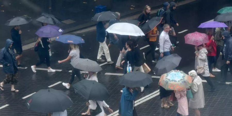 Fussgänger schützen sich mit Regenschirmen vor starkem Regen. Der Niederschlag bringt angesichts der anhaltenden Buschbrände in New South Wales etwas Entlastung für die Einsatzkräfte. Foto: Bianca De Marchi/AAP/dpa