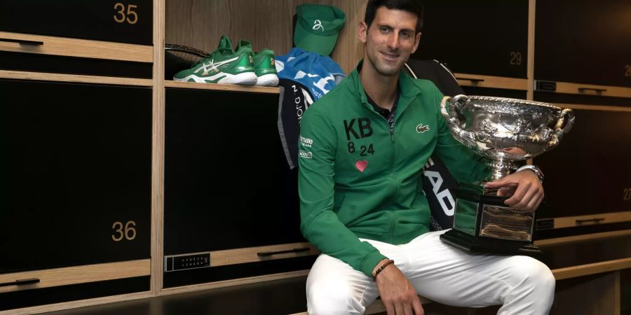 Novak Djokovic posiert mit dem Pokal der Australian Open in der Garderobe.