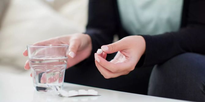 Frau mit Glas und Wasser und Tabletten zur Einnahme