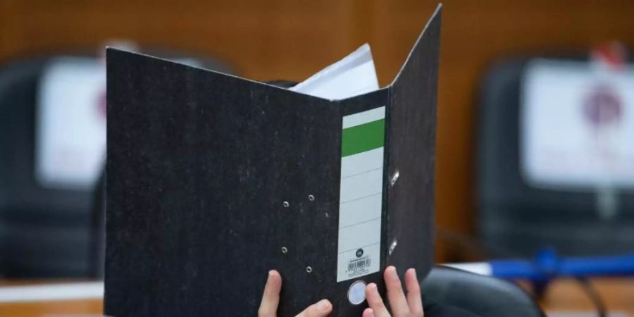 Der Angeklagte verbirgt sein Gesicht hinter einem Aktendeckel. Foto: Boris Roessler/dpa