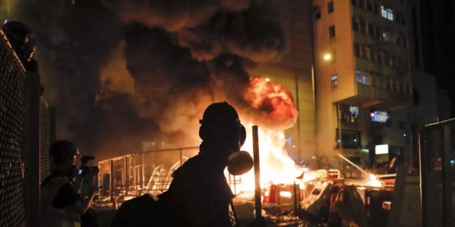 Ein Demonstrant mit einer Gasmaske steht vor den lodernden Flammen eines Feuers in Hongkong. Foto: Kin Cheung/AP