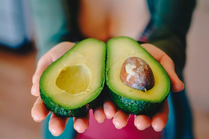 Eine Frau zeigt eine halbierte Avocado. Avocado