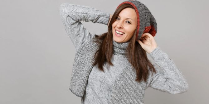 Lächelnde Frau mit grauem Pullover, Mütze und Schal