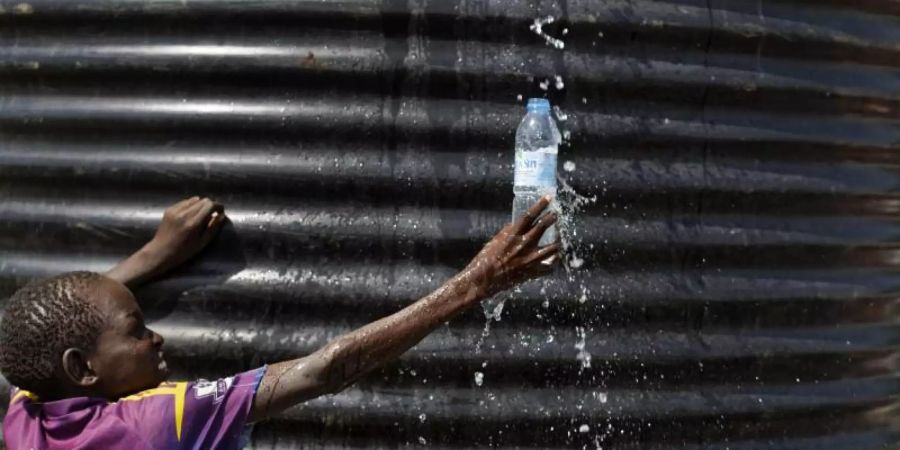 Ein Flüchtlingsjunge aus dem Südsudan fängt in einer Empfangsstelle für Flüchtlinge in Imvepi (Uganda) mit einer Flasche Wasser auf. Foto: Ben Curtis/AP/dpa