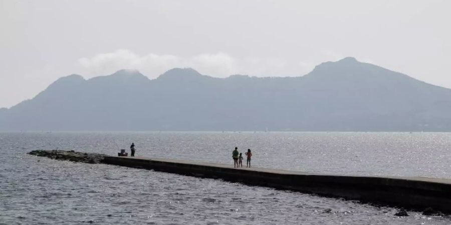 Menschen sonnen sich im Hafen von Pollença auf der Insel Mallorca. Branchenschätzungen zufolge werden über Ostern rund 40.000 Deutsche ihren Urlaub auf Mallorca verbringen. Foto: Clara Margais/dpa
