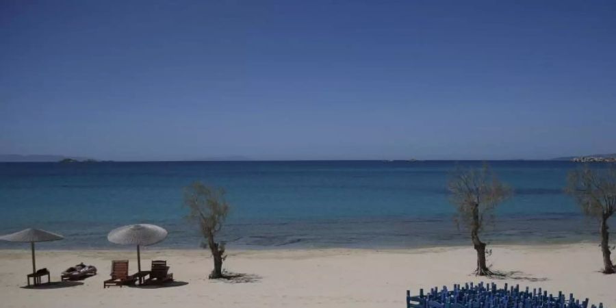 Ein Tourist geniesst die Sonne, während Tavernenstühle am Strand von Plaka auf der Ägäisinsel Naxos gelagert werden. Foto: Thanassis Stavrakis/AP/dpa