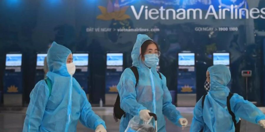 Passagiere in voller Schutzkleidung gegen das Coronavirus gehen durch den Flughafen Hanoi. Foto: Hau Dinh/AP/dpa