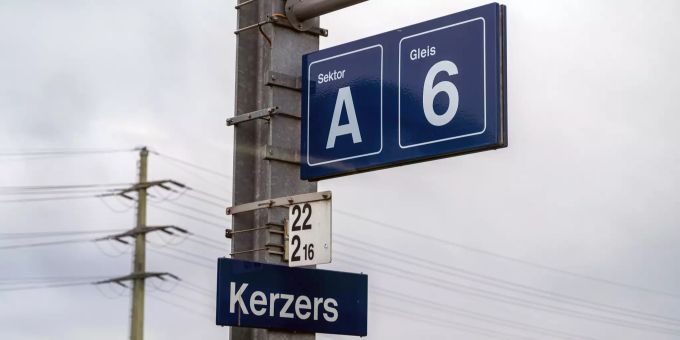 Namensschild «Kerzers» auf dem Gleis 6 und Stromast im Hintergrund - Kerzers Namensschild «Kerzers» auf dem Gleis 6 und Stromast im Hintergrund - Kerzers
