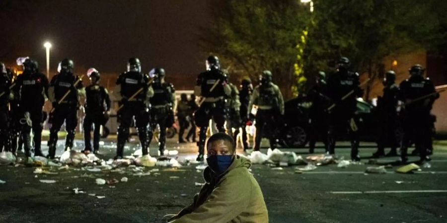 Ein Demonstrant sitzt in Minnesota als Protest auf einer Strasse vor einer Reihe von Bereitschaftspolizisten. Foto: Imagespace/imageSPACE via ZUMA Wire/dpa