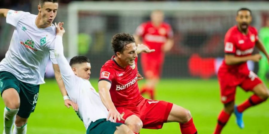 Leverkusens Julian Baumgartlinger (r) wird von Bremens Milot Rashica zu Fall gebracht, links läuft Bremens Marco Friedl. Foto: Rolf Vennenbernd/dpa