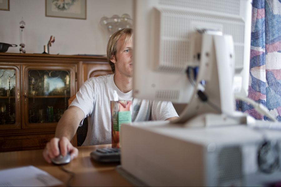 Arbeit: junger Mann sitzt vor dem Computer und bewirbt sich.