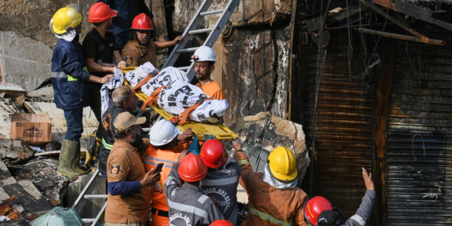 Feuerwehrleute transportieren eine Leiche, nachdem sie sie aus den Trümmern eines abgebrannten Gebäudes eines mehrstöckigen Einkaufszentrums nach einem Großbrand geborgen haben. Fot...