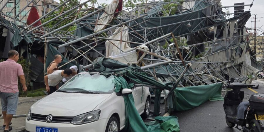 dpatopbilder - Menschen blicken in der ostchinesischen Provinz Zhejiang in das Innere eines Autos, das von einem umgestürzten Gerüst eingeklemmt wurde, nachdem der Taifun «Dolphin» ...