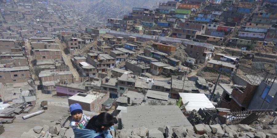 ARCHIV - Eine Frau trägt ihr Kind am Rücken und geht über Steine zu einem Haus in Lima, in dem Essen verteilt wird. Foto: Gian Masko/dpa