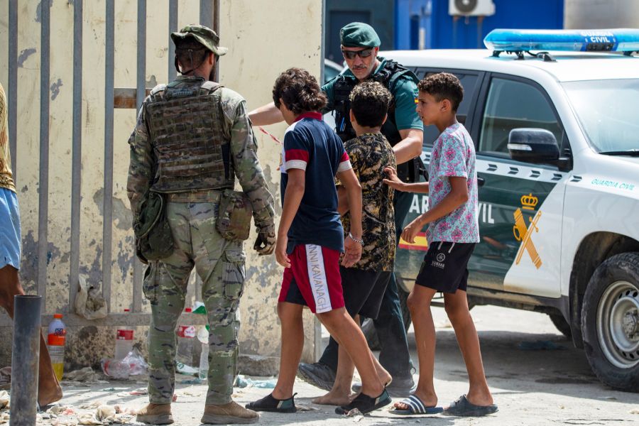 Ein Angehöriger der Guardia Civil und ein Soldat begleiten mehrere Jugendliche an einem Grenzposten in Ceuta.