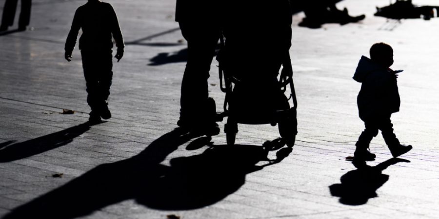 ARCHIV - Zwei Kinder und ein Mann mit einem Kinderwagen laufen im Gegenlicht der Sonne und werfen dabei lange Schatten auf den Boden. Foto: Julian Stratenschulte/dpa/Archivbild
