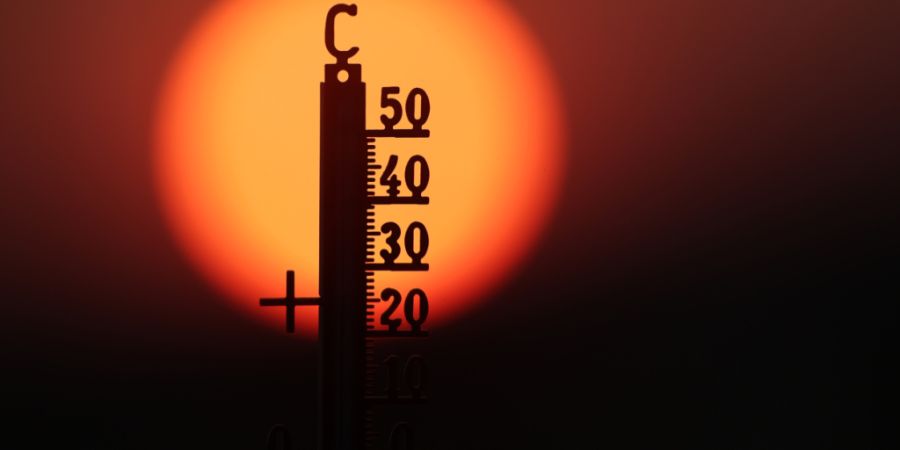 ARCHIV - Hinter einem Thermometer geht am Morgen die Sonne auf. Foto: Thomas Warnack/dpa