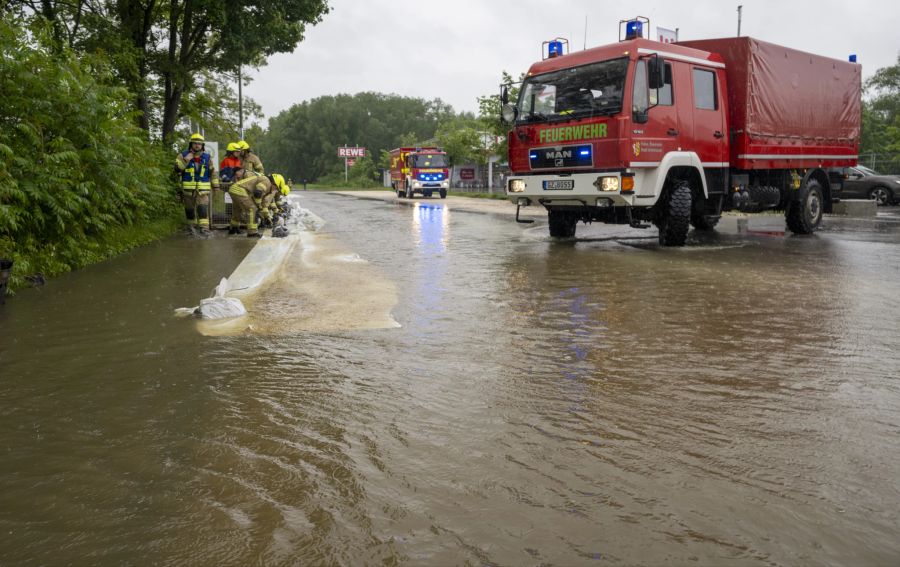 01.06.2024, Bayern, Ichenhausen: Feuerwehrleute errichten Barrieren an einer von der Günz überfluteten Strasse, um das Wasser aus der Stadt fernzuhalten.