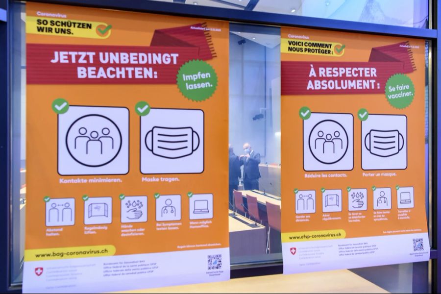 Plakate mit den aktuell gültigen Corona-Massnahmen, während im Hintergrund Bundesrat Alain Berset, rechts, mit Patrick Mathys spricht, dem Leiter Sektion Krisenbewältigung und internationale Zusammenarbeit im BAG, links, nach einer Medienkonferenz am 3. Dezember 2021.