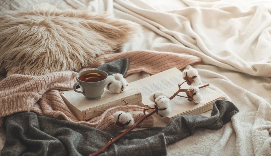 Weiche Decken, flauschige Kissen, sanfte Farbtöne, ein Buch und eine Tasse Tee.