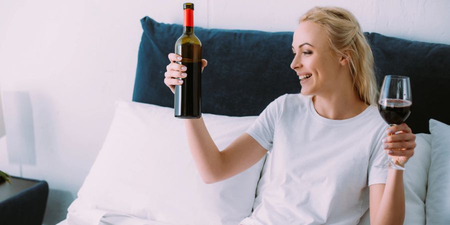 Lächelnde Frau geniesst Wein in Bett