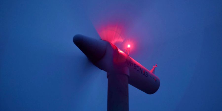 Die Rotoren einer beleuchteten Windkraftanlage drehen sich vor Sonnenaufgang.