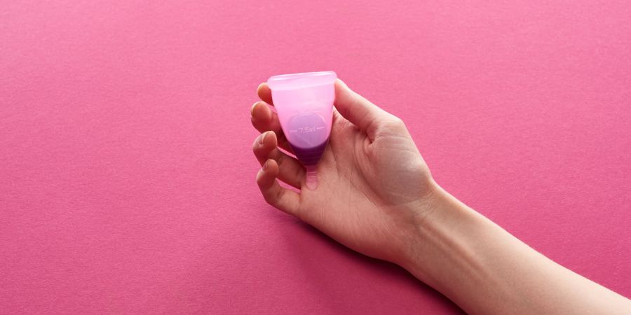 Frauenhand hält menstruationstasse, rosa hintergrund