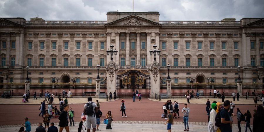 Touristen stehen vor den Toren vom Buckingham Palast in London.