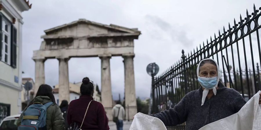 Eine Frau mit Mund-Nasen-Schutz verkauft eine Decke vor dem Tor der antiken römischen Agora in Plaka, einem Stadtteil von Athen. Foto: Petros Giannakouris/AP/dpa