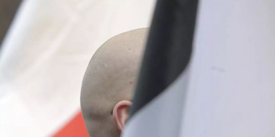 En Mann mit geschorenem Kopf zwischen schwarz-weiss-roten Fahnen: Momentaufnahme einer Demo. Foto: picture alliance / dpa