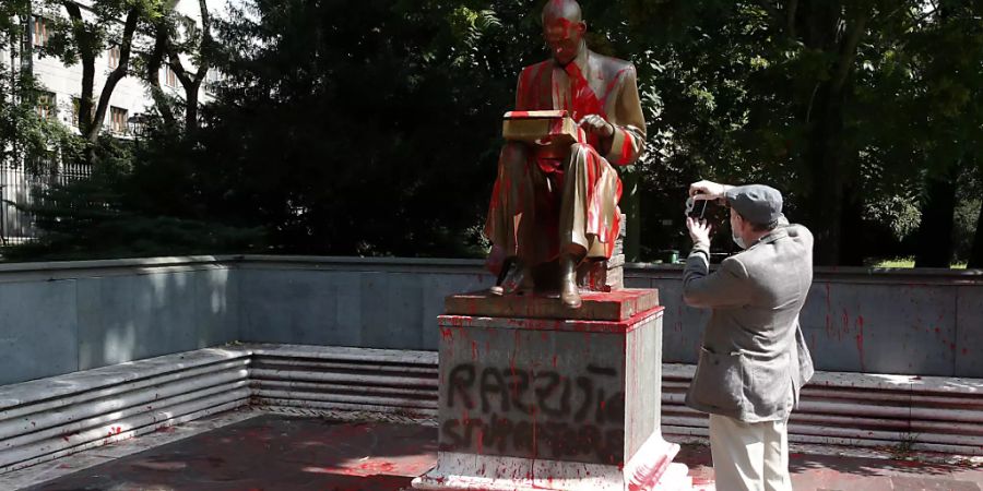 Ein Mann fotografiert die von Demonstranten mit roter Farbe beworfene Statue des verstorbenen italienischen Journalisten Indro Montanelli in Mailand. Foto: Antonio Calanni/AP/dpa