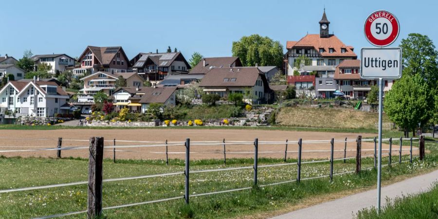 Ortsschild Uttigen mit Blick auf das alte Schulhaus und das Oberdorf.